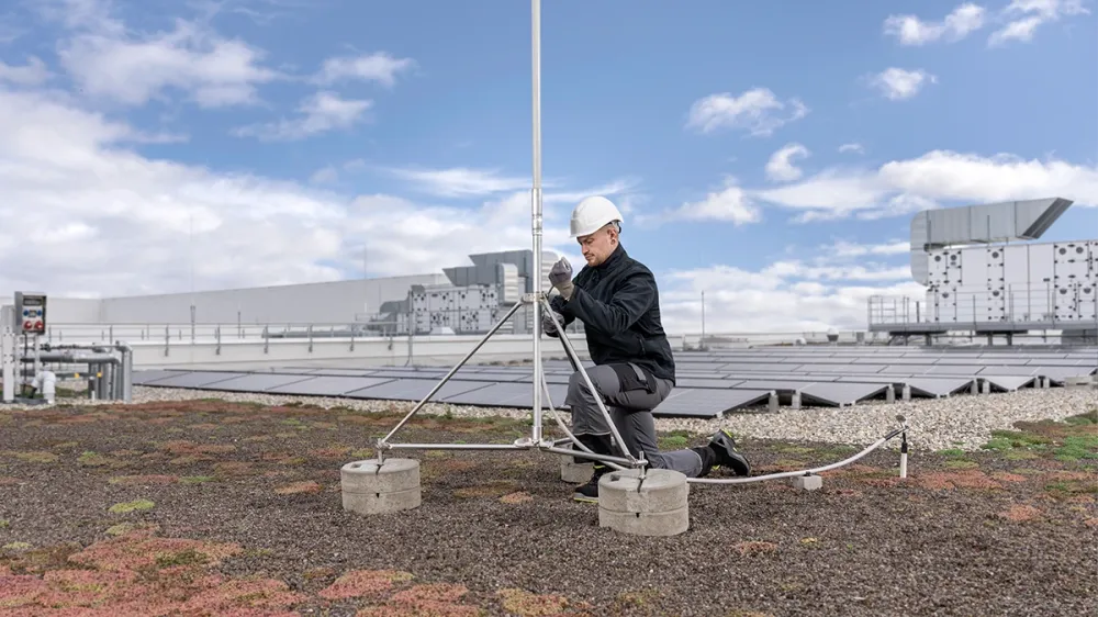 Mann mit Schutzhelm montiert Blitzableiter auf Gründach mit Solaranlage.