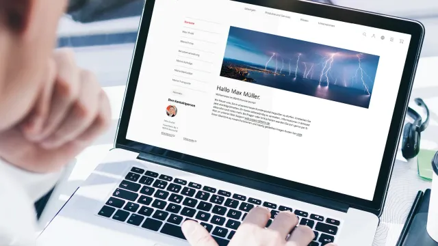 A person using a laptop, viewing a webpage featuring a profile and a header image of wind turbines against a cloudy sky.