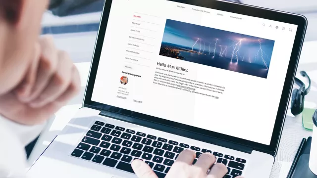 A person using a laptop, viewing a webpage featuring a profile and a header image of wind turbines against a cloudy sky.