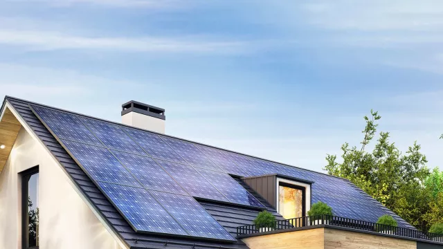 Modern single-family house with rooftop solar panels, large windows, and surrounding trees under a clear blue sky.