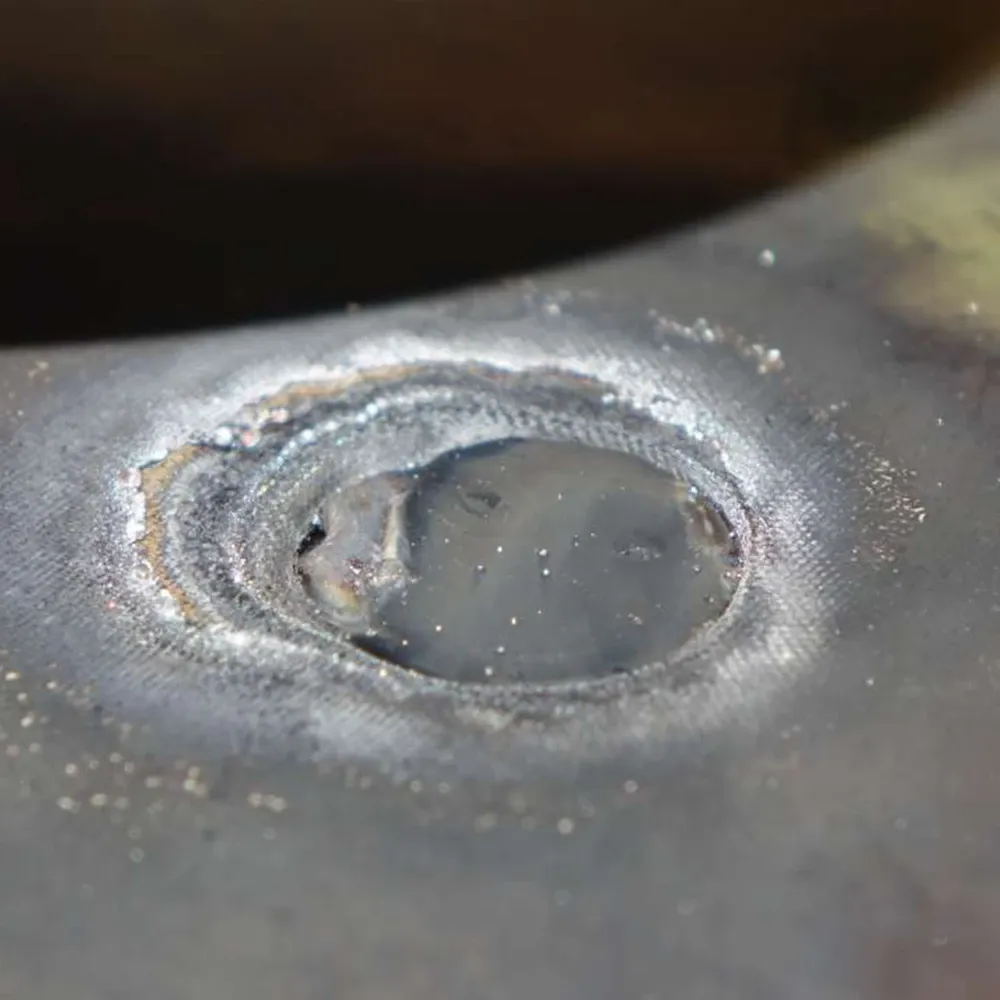 Close-up of a circular weld spot on a metal surface with heat marks, rough edges, and small metal particles.