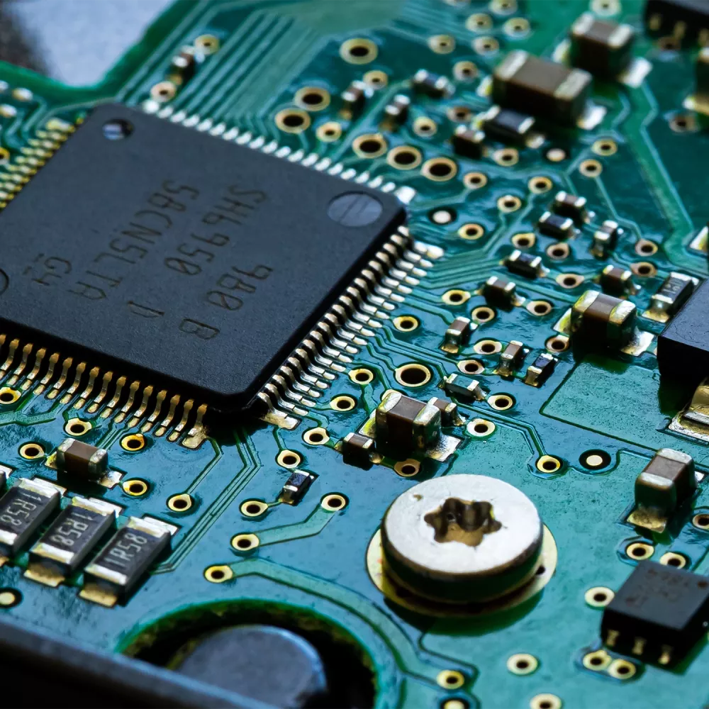 Close-up of a green printed circuit board with a black microchip, gold pins, resistors, capacitors, and a metal screw mount.