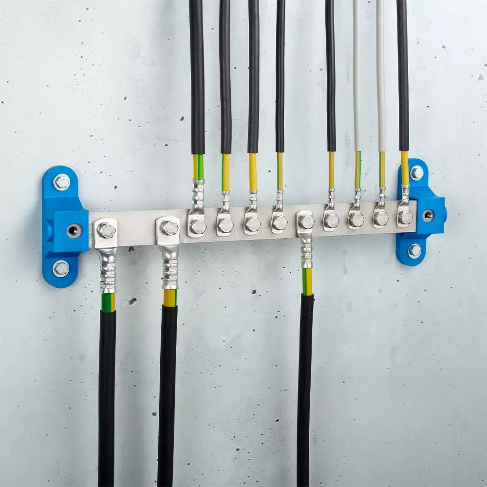 Metal grounding bar mounted on a wall with multiple black and green-yellow cables secured by bolts and two blue mounting brackets.