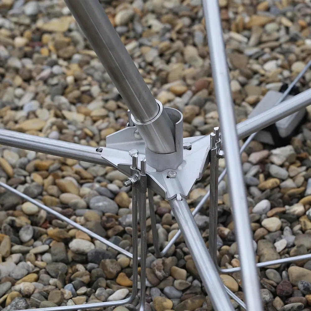 Person aligning metal rods with a spirit level on a gravel surface, hands visible near concrete blocks. Close-up of a metal joint connecting angled rods with bolts and clamps, installed on a gravel surface.