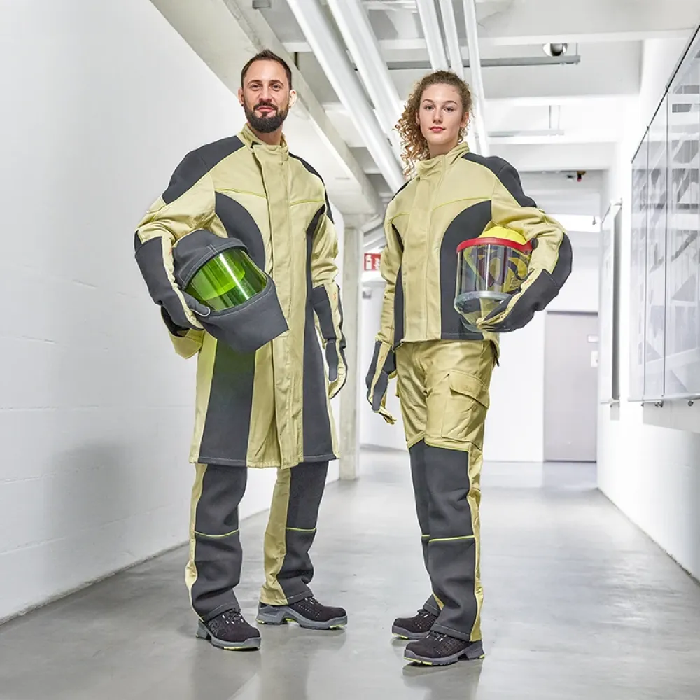 Two electricians in protective workwear stand in an industrial corridor, holding helmets with visors as part of modern personal protective equipment.