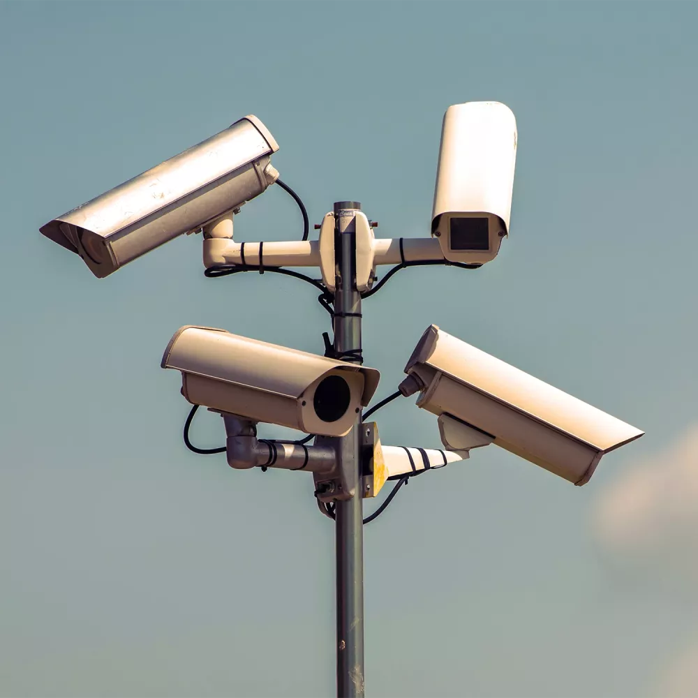 Outdoor surveillance pole with multiple security cameras mounted in different directions against a clear sky.