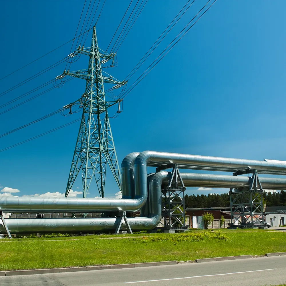 Industrial pipeline installation beneath a high-voltage transmission tower with overhead power lines under a clear blue sky.