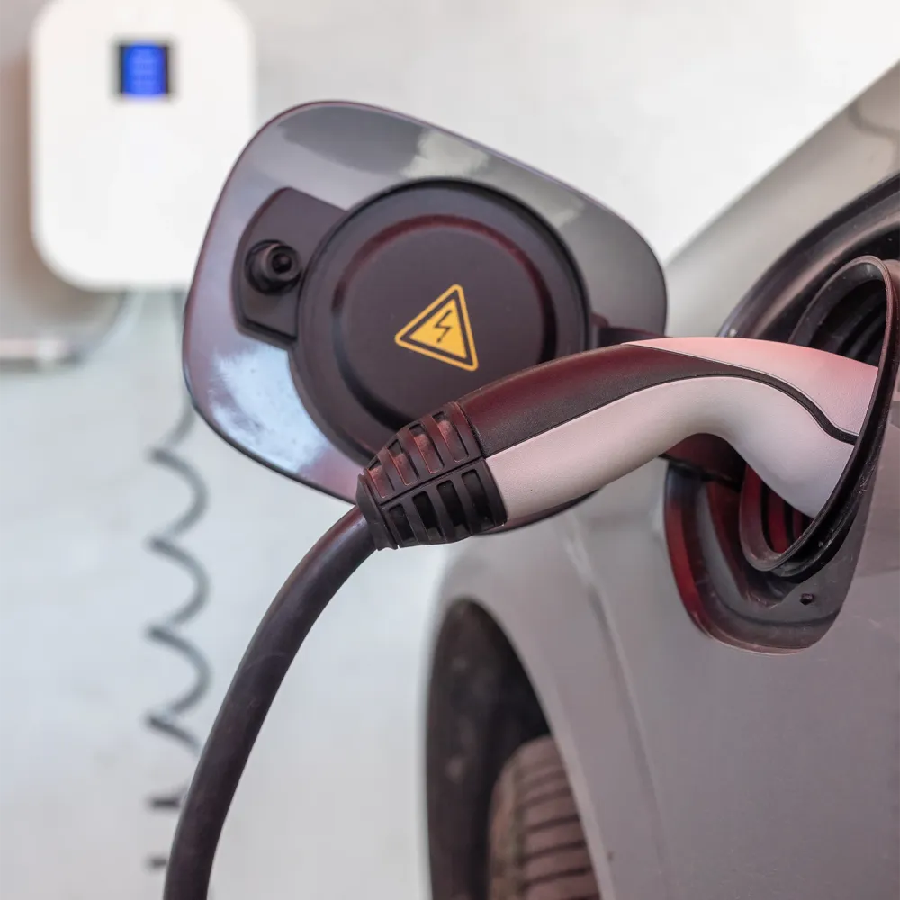 Close-up of an electric car charging connector plugged into the vehicle’s charging port, with a high-voltage warning symbol visible.