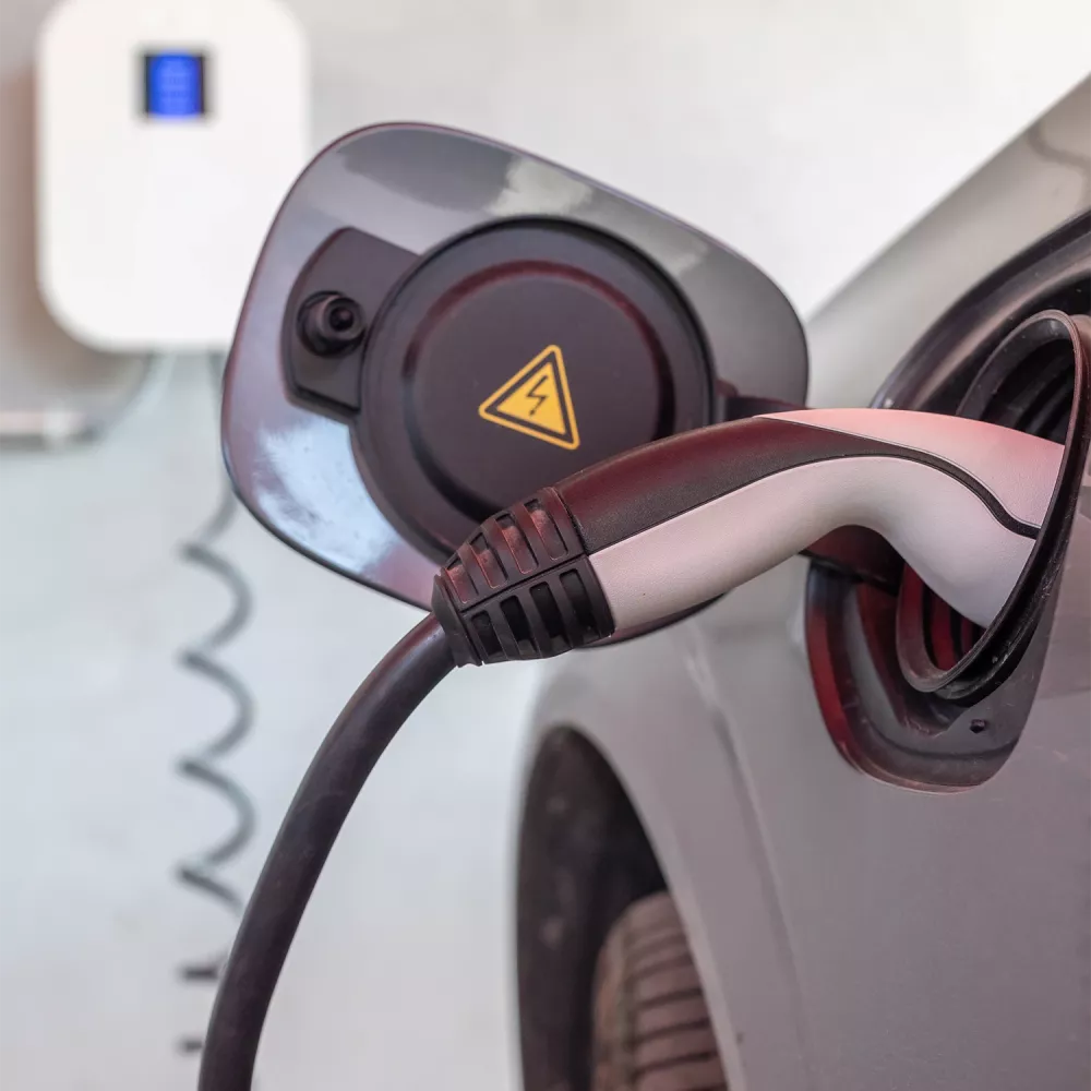 Close-up of an electric car charging connector plugged into the vehicle’s charging port, with a high-voltage warning symbol visible.