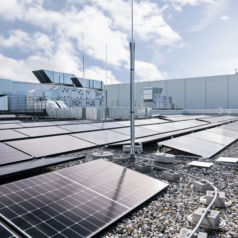 Rooftop photovoltaic system with solar panels, lightning protection mast, and cable routing on a commercial building roof under a cloudy sky.