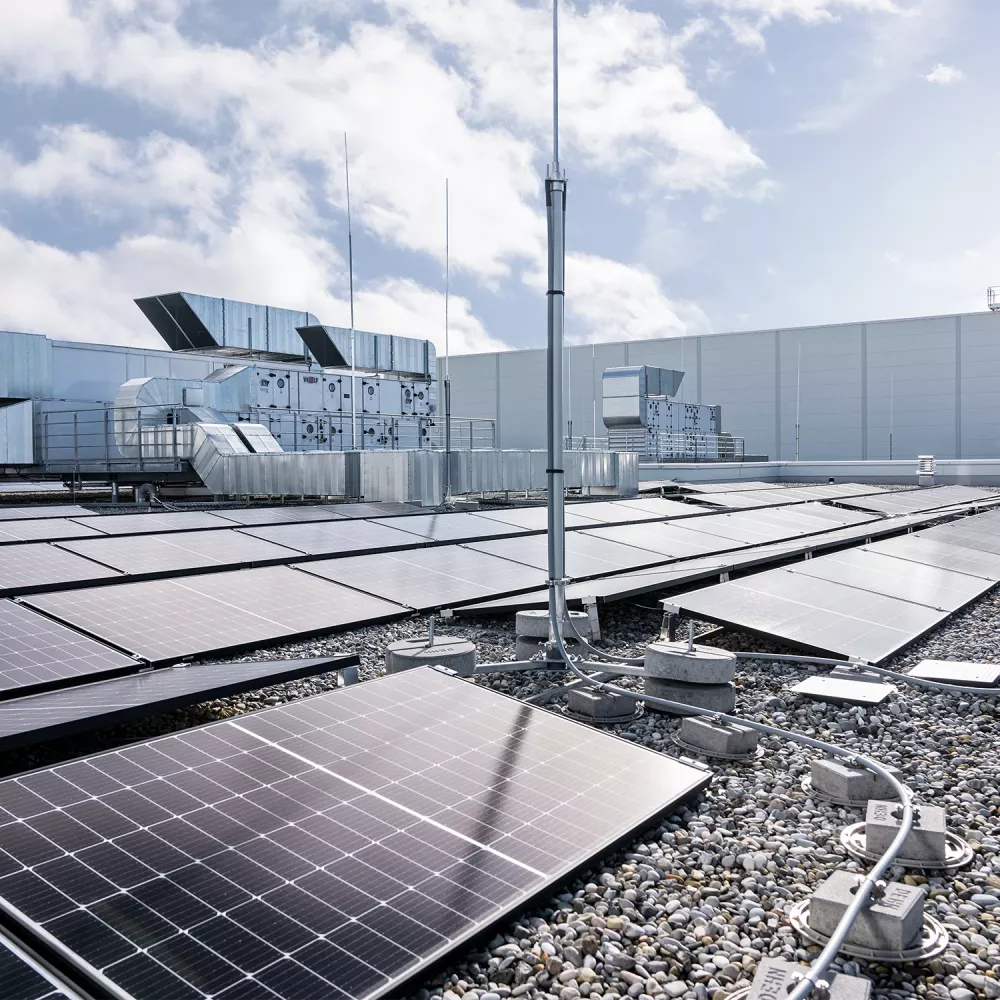 Rooftop photovoltaic system with solar panels, lightning protection mast, and cable routing on a commercial building roof under a cloudy sky.