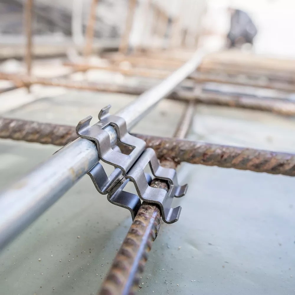 Close-up of a metal grounding clamp connecting a steel conductor to reinforcing rebar embedded in a concrete foundation slab.