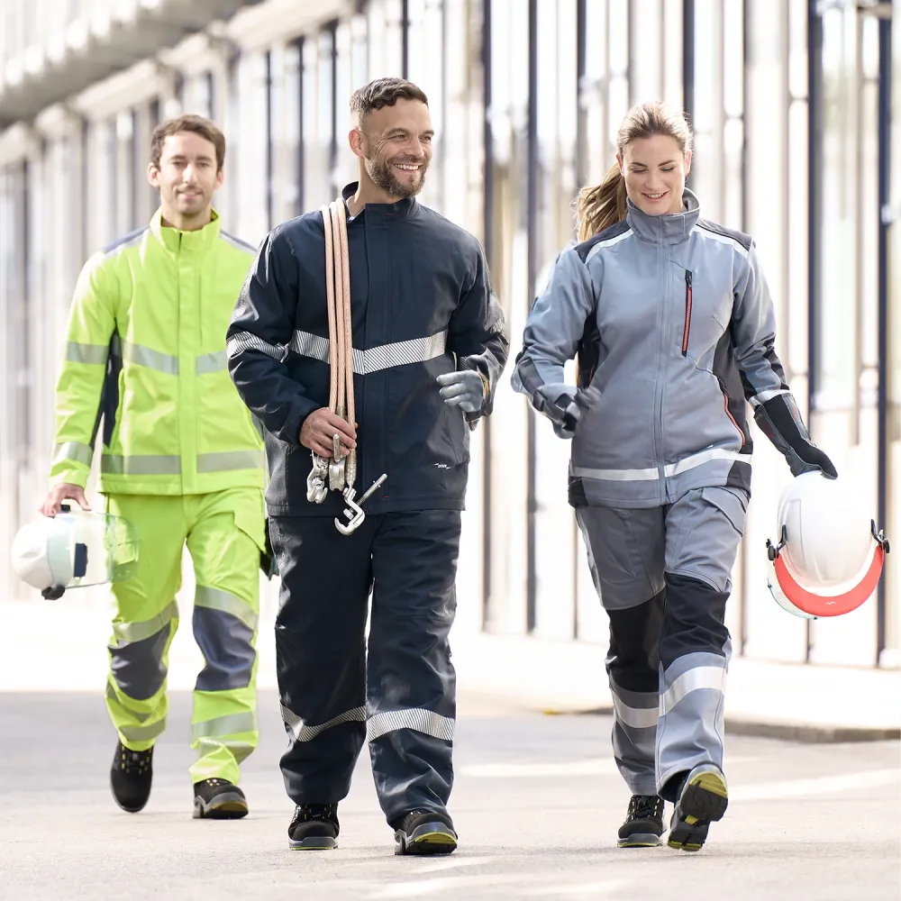 Three technicians in protective workwear walking through an industrial facility, carrying helmets and safety equipment.