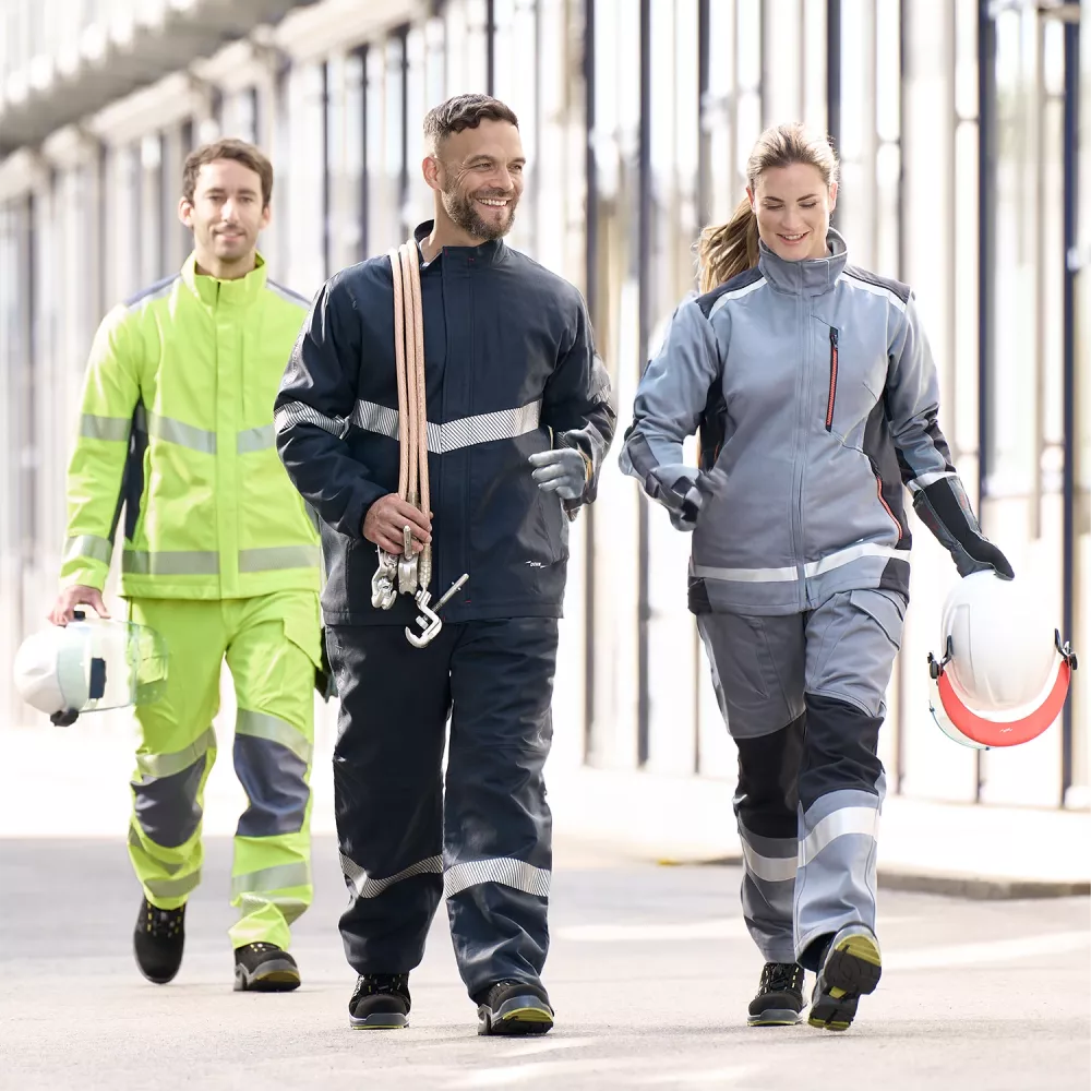 Three technicians in protective workwear walking through an industrial facility, carrying helmets and safety equipment.