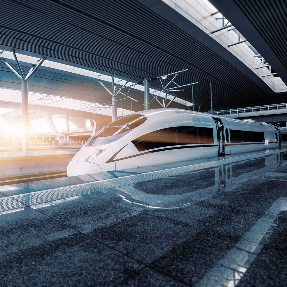 White high-speed train at a modern station platform, sunlight streaming through the glass roof and reflecting on the polished floor.