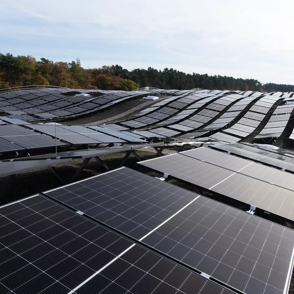 Large industrial photovoltaic installation with rows of solar panels on curved rooftop landscape near forest.