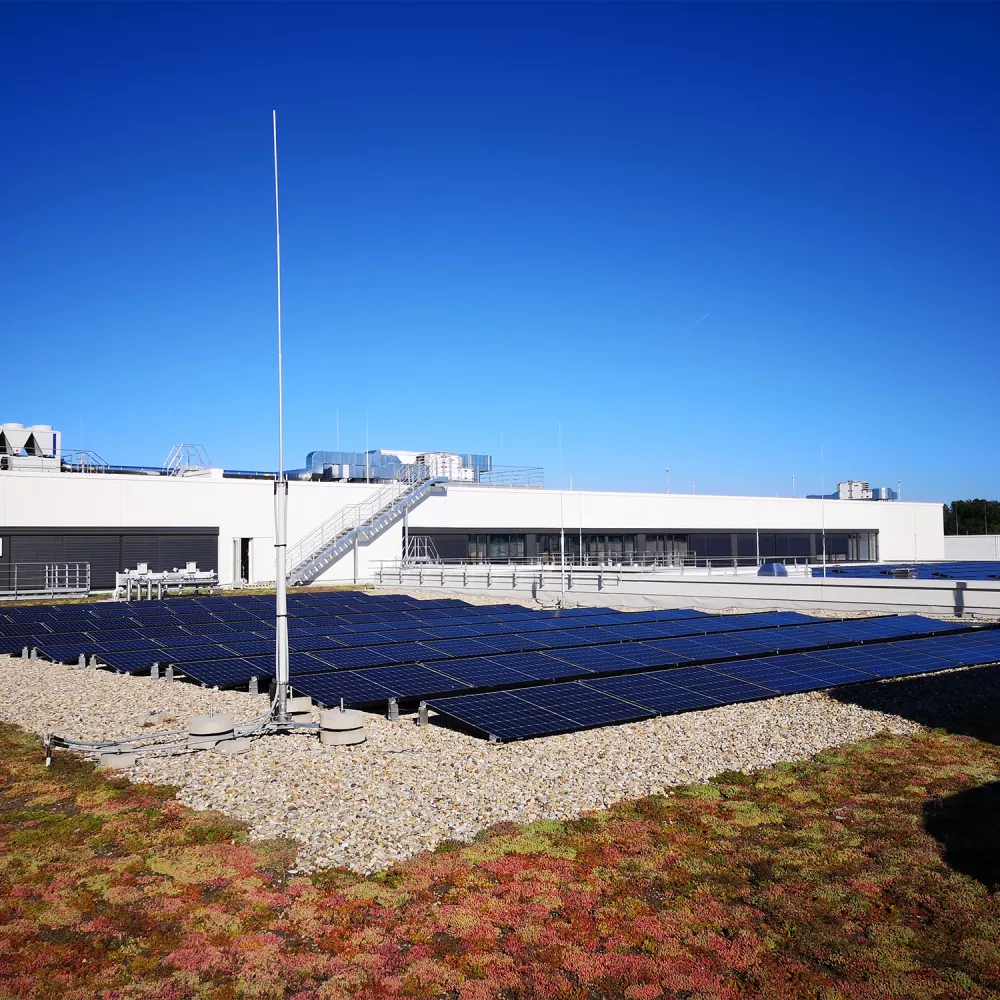 Rooftop solar panels installed on industrial building with lightning protection masts under clear blue sky.