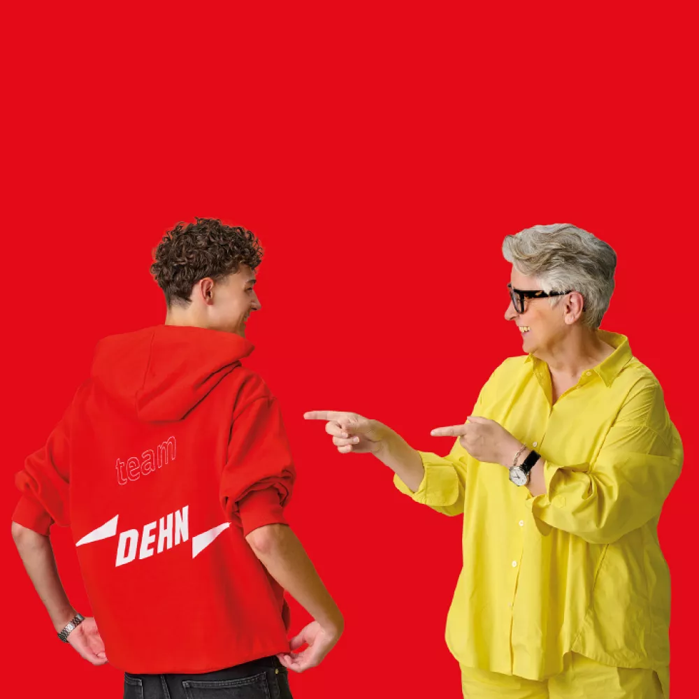 Person in yellow shirt pointing at person wearing red hoodie with 'team DEHN' text on back against red background