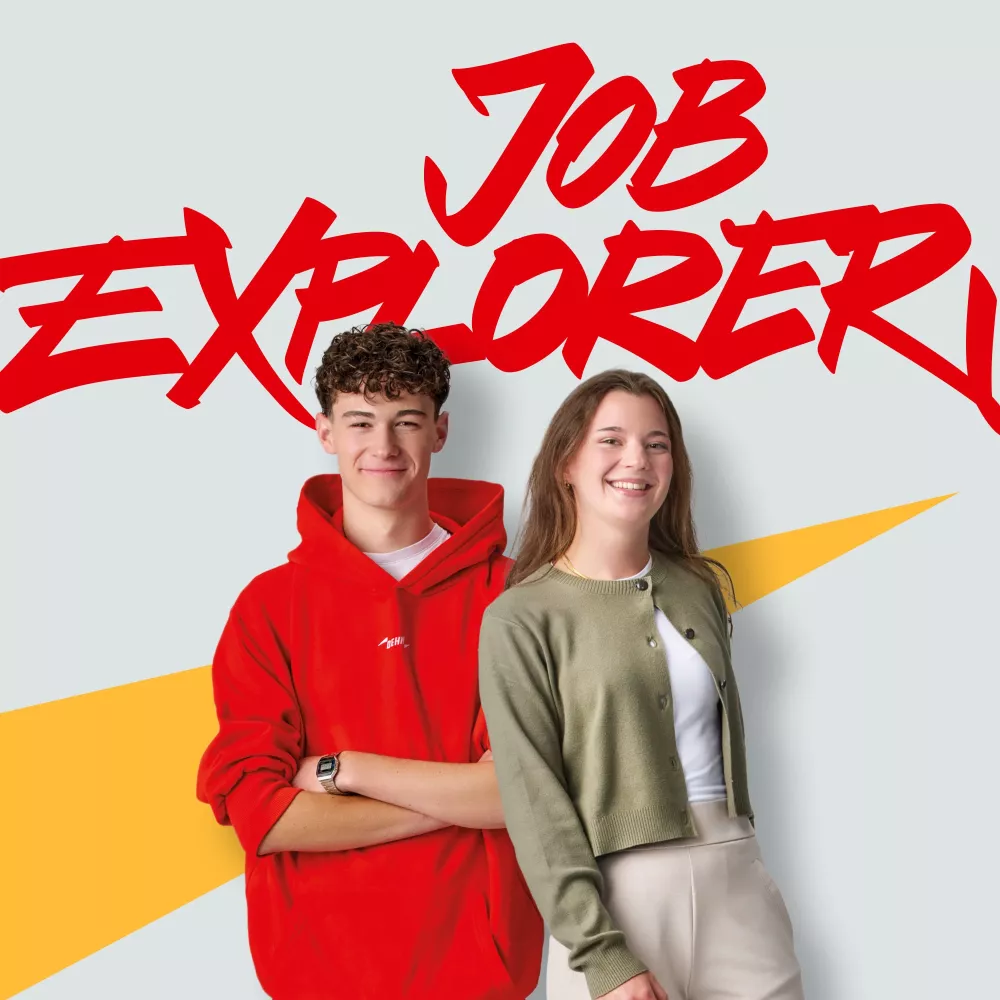 Two young people smiling at the camera are standing in front of a wall featuring Job Explorer graffiti
