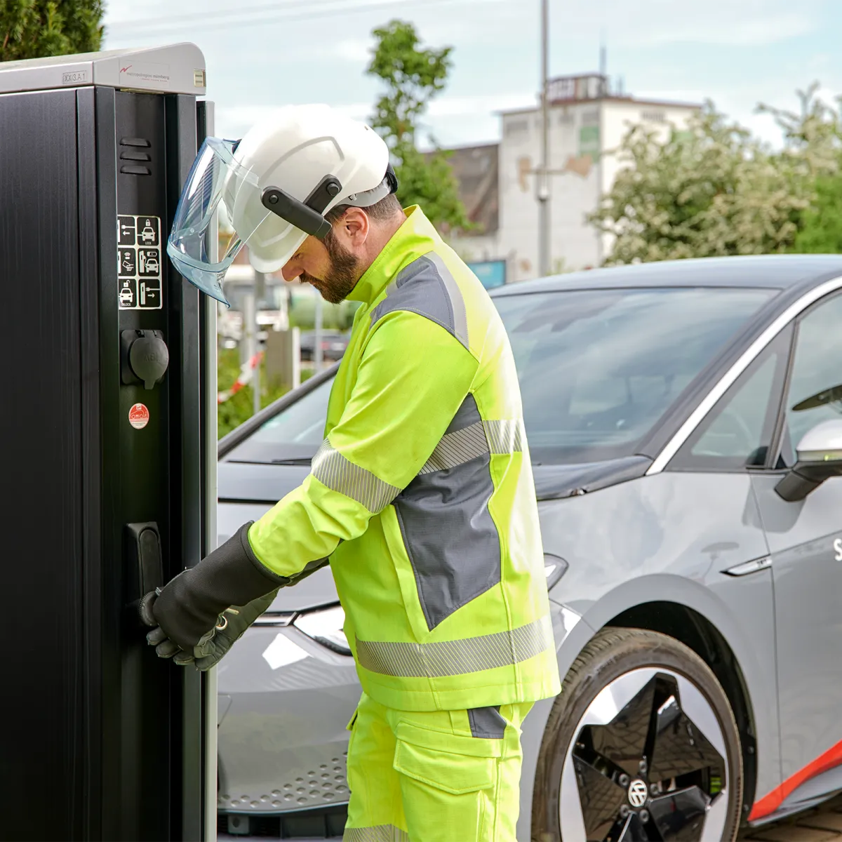 Person in Sicherheitsweste und Helm, die ein Elektrofahrzeug an eine Ladestation anschließt.