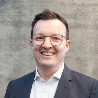 Portrait von Simon Thaler vor einem grauem Hintergrund.