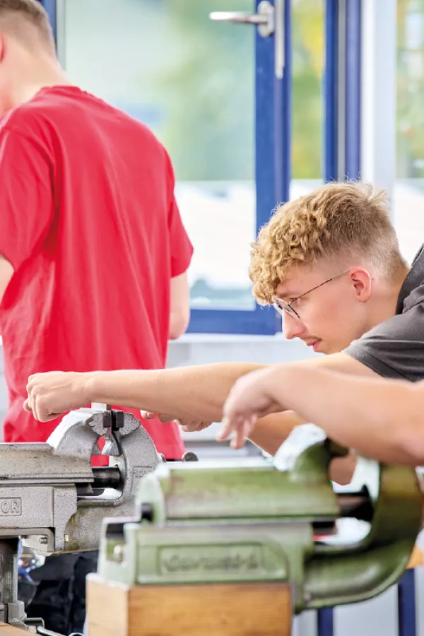 Three people working with metalworking machines in a workshop.