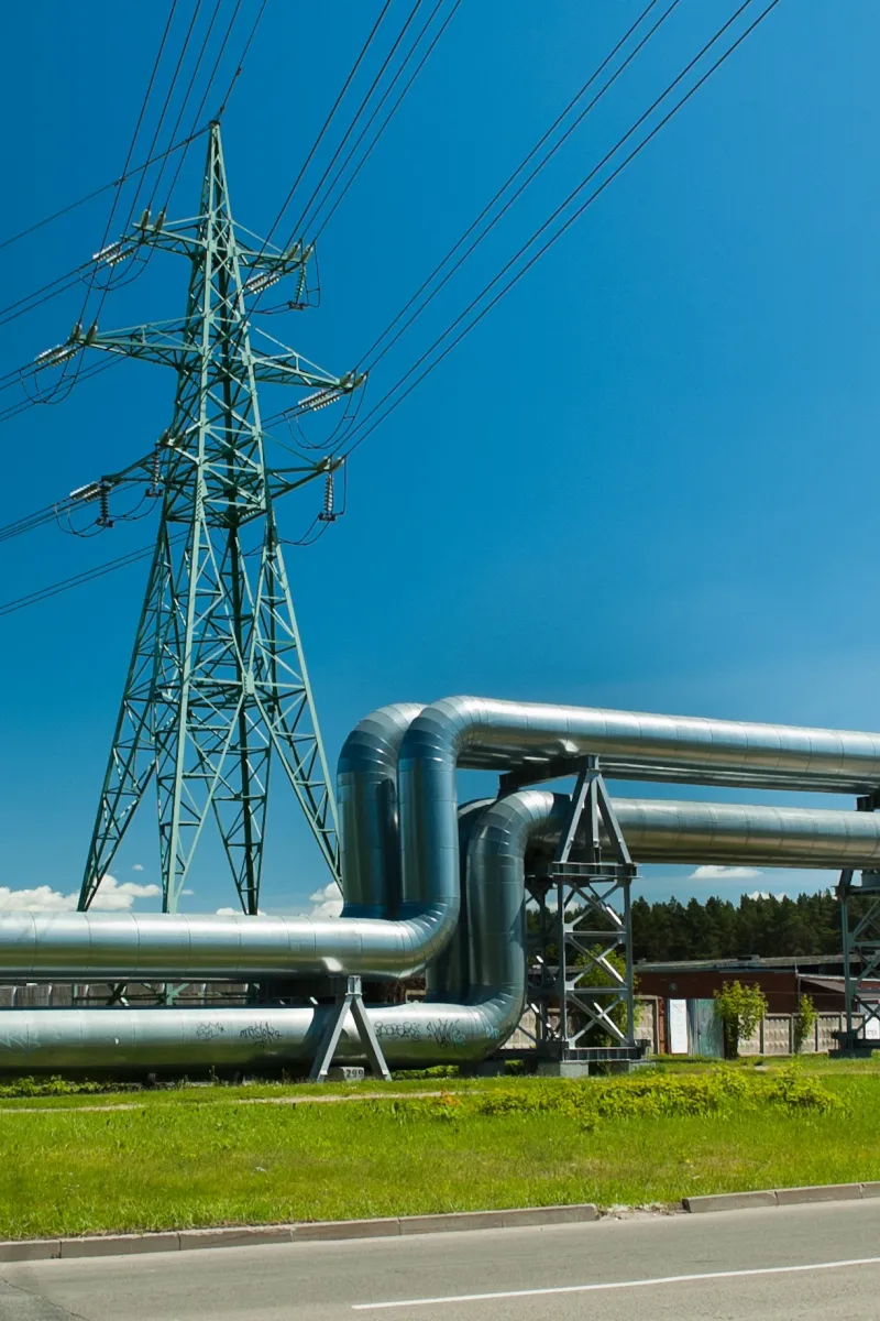 Hochspannungsleitung und Pipeline auf grüner Wiese vor blauem Himmel.