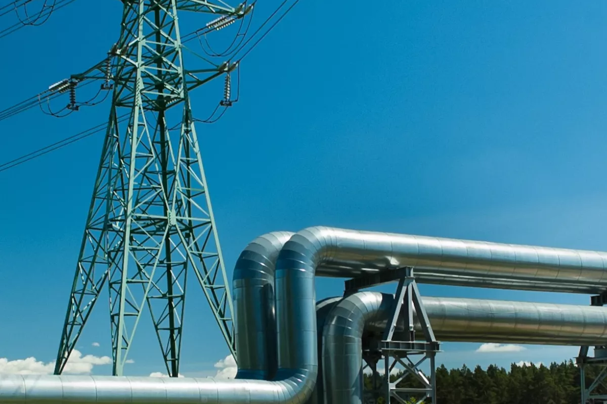 Hochspannungsleitung und Pipeline auf grüner Wiese vor blauem Himmel.