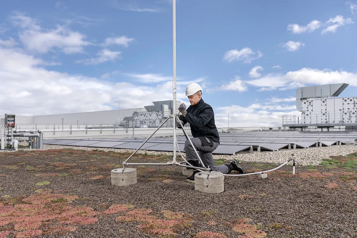 Mann mit Schutzhelm montiert Blitzableiter auf Gründach mit Solaranlage.