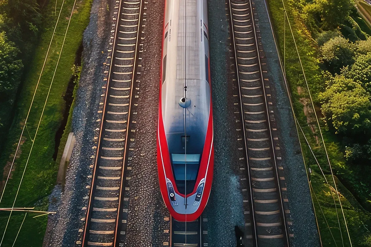 Top-down aerial view of a red high-speed train traveling on railway tracks, surrounded by green vegetation on both sides.