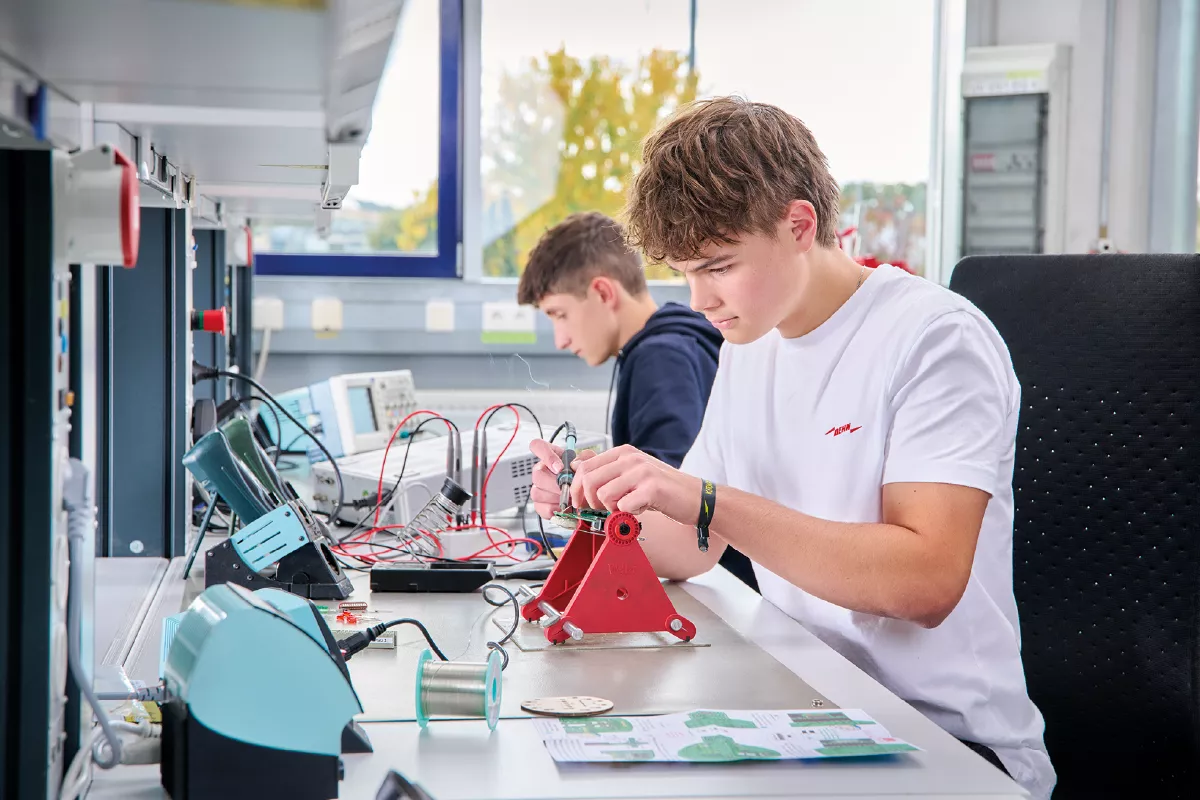 Two young men working with electronic equipment and wiring at a laboratory bench.